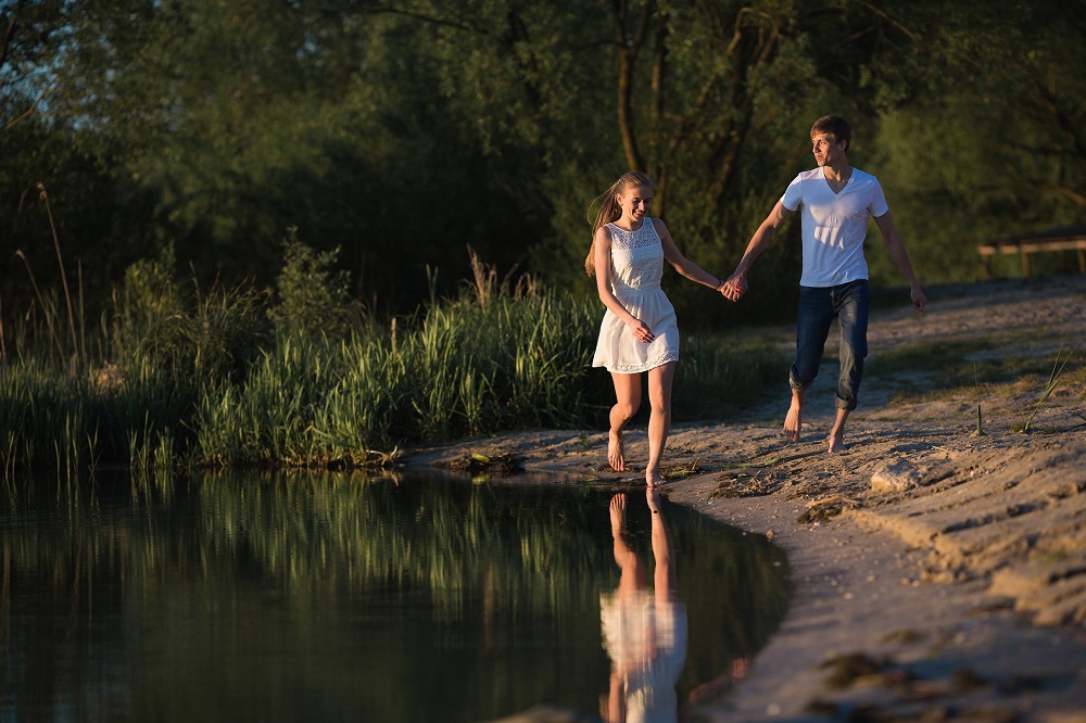 teen couple in love running beside a lake Couple in sunrise on the beach