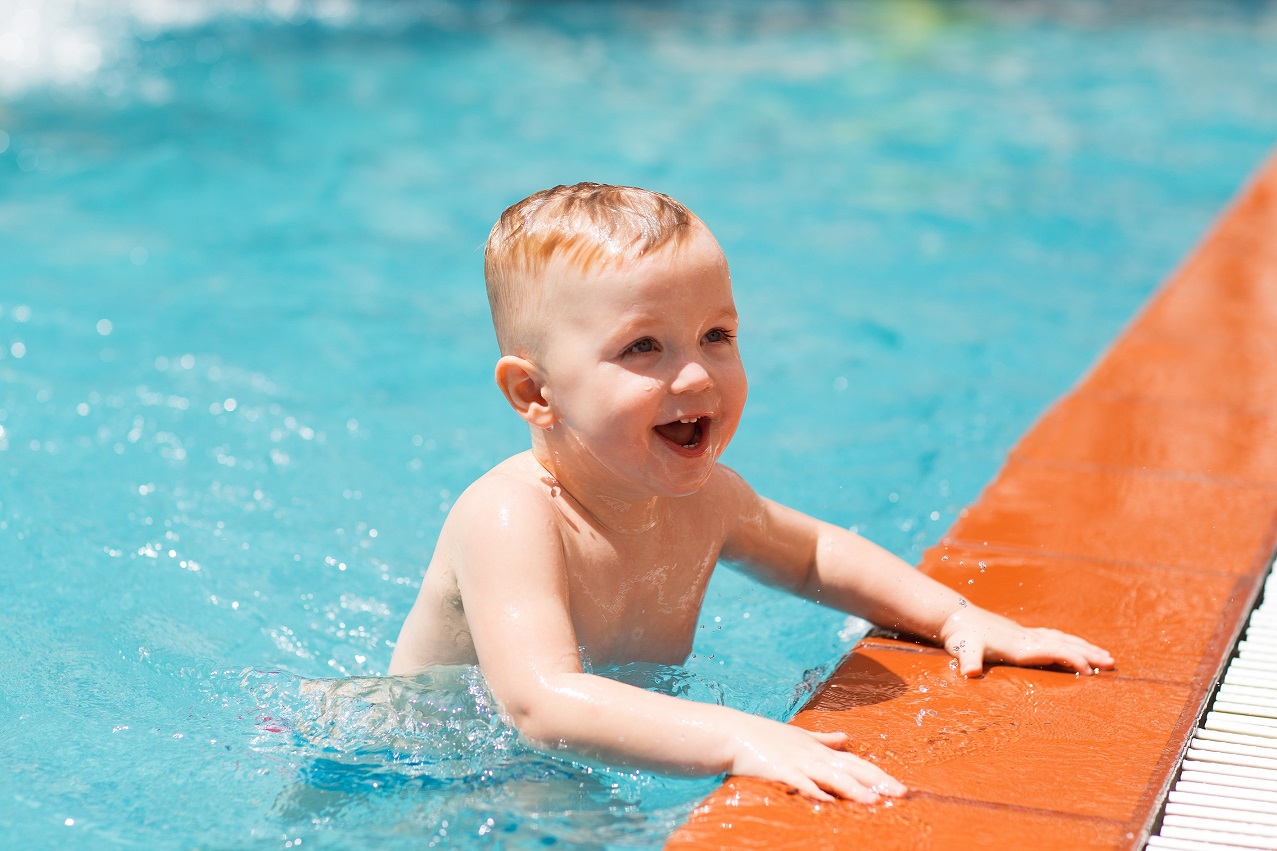 Portrait of happy little Caucasian boy swimming in outdoor pool and smiling. Summer vacation, sport, health and childhood concept