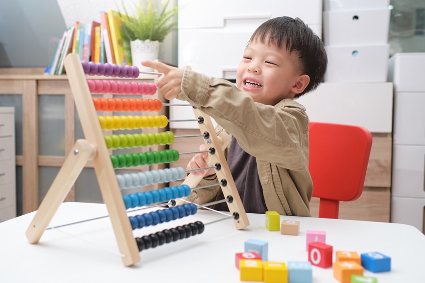 Cute little asian kindergarten 4 years old boy using the abacus with beads and wooden brick with numbers to learn how to count indoor at home, Use an Abacus to teach maths for little kids concept