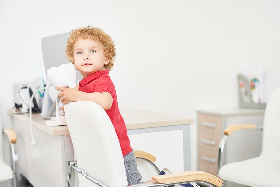 Portrait of cute little boy with blonde curly hair looking away pensively while playing at dental office