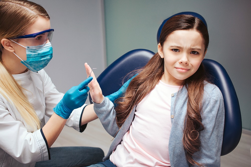 Girl sit in chair in dentist's room. Doctor look at her. Scared girl. She refuse treatment