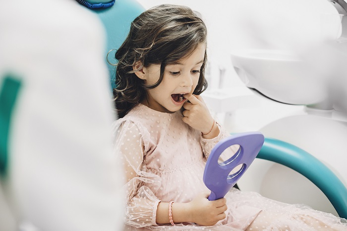 Lovely little girl looking at her teeth after surgery in a pediatric stomatology.